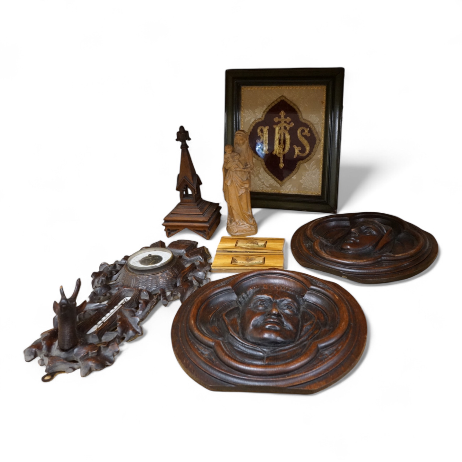 A pair of Gothic revival oak wall plaques, a Black Forest carved barometer, a Virgin and child figure, an IHS embroidered panel, two straw worked panels and a carved finial, barometer 47cm high